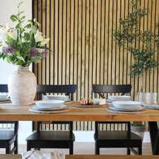 A dining room with a wood-panelled wall behind a long set dining table with a large vase of flowers