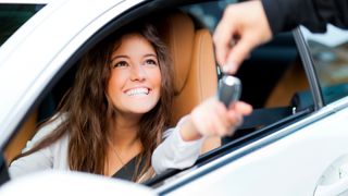 Smiling women sat in a car reaching through the open window to accept a car key
