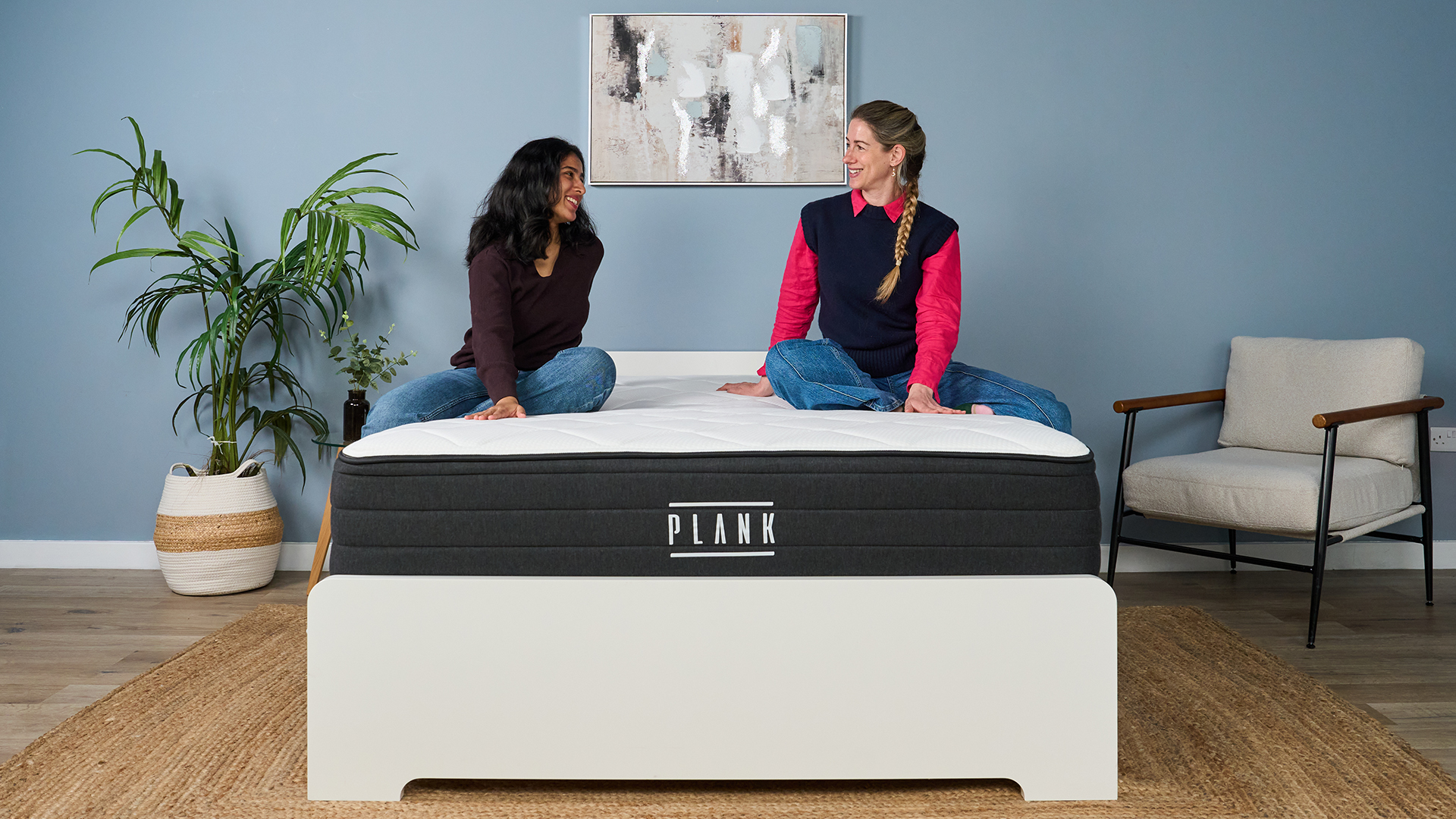 Mattress testers Becky George and Nicola Appleton sit on the Plank Firm Luxe mattress on a bed frame in the Tom's Guide sleep studio