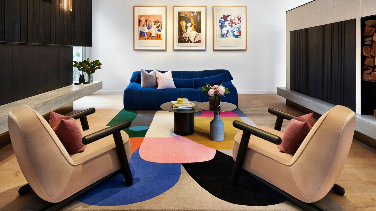 A blue couch with pink cushions opposite two cream colored accent chairs in a living room 