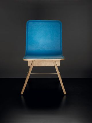 Close up of a small wooden chair with blue seat, black floor and grey backdrop