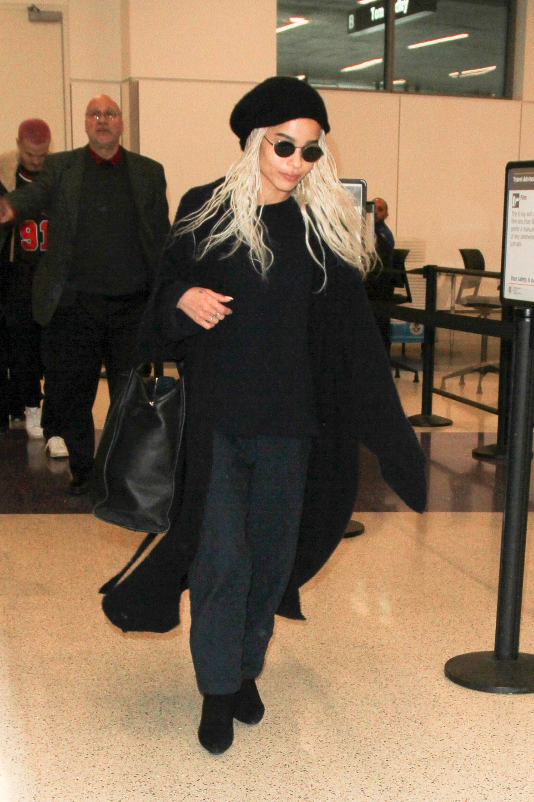 Zoë Kravitz wearing a black jumper, black joggers, blaxk coat, black boots and beret at the airport.