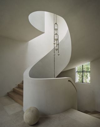 A neutral toned spiralling staircase with a long pendant light