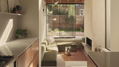 conversation pit in modern extension with fireplace, exposed timber ceiling details, galley kitchen, and L-shaped sofa