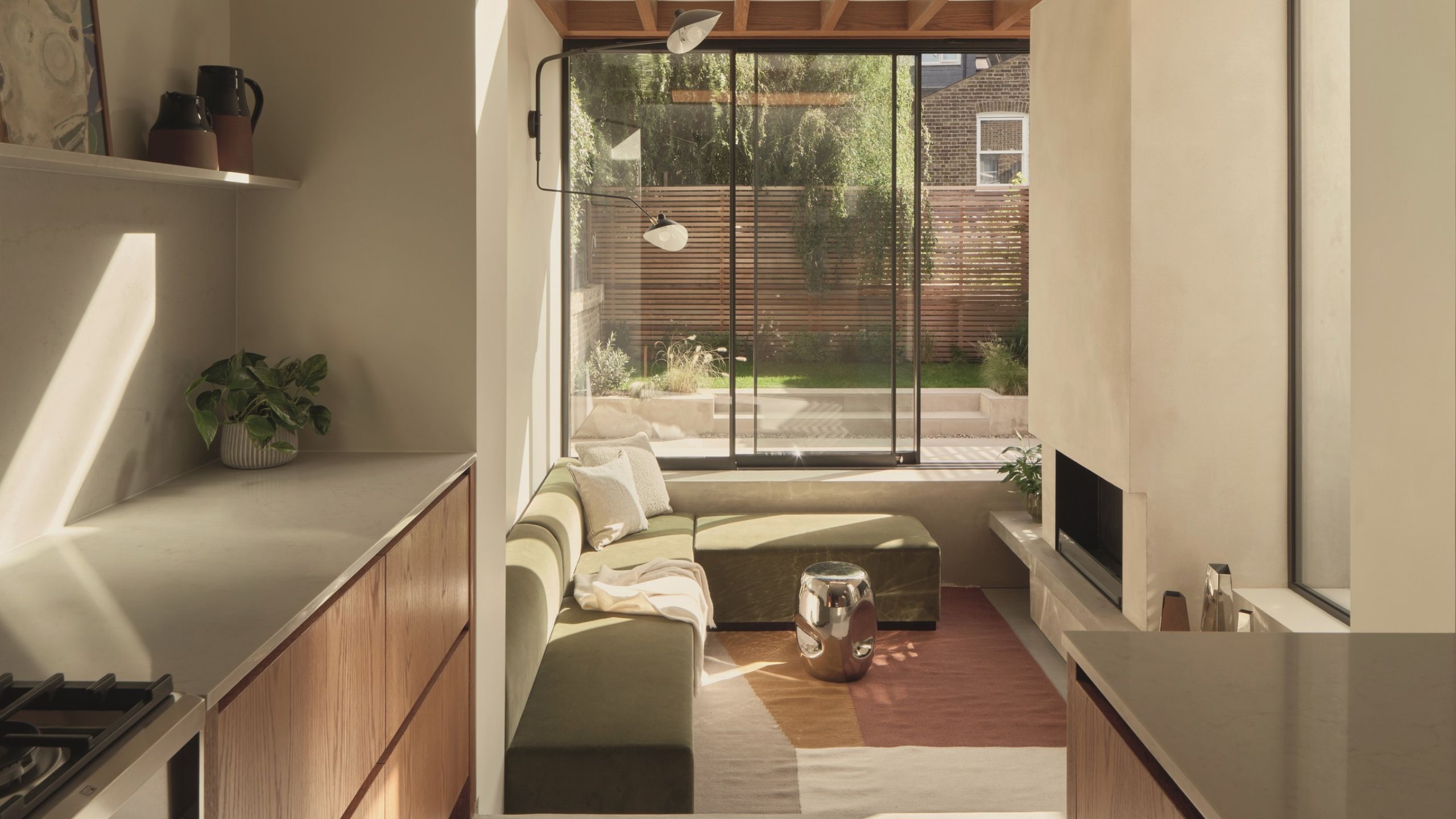 conversation pit in modern extension with fireplace, exposed timber ceiling details, galley kitchen, and L-shaped sofa