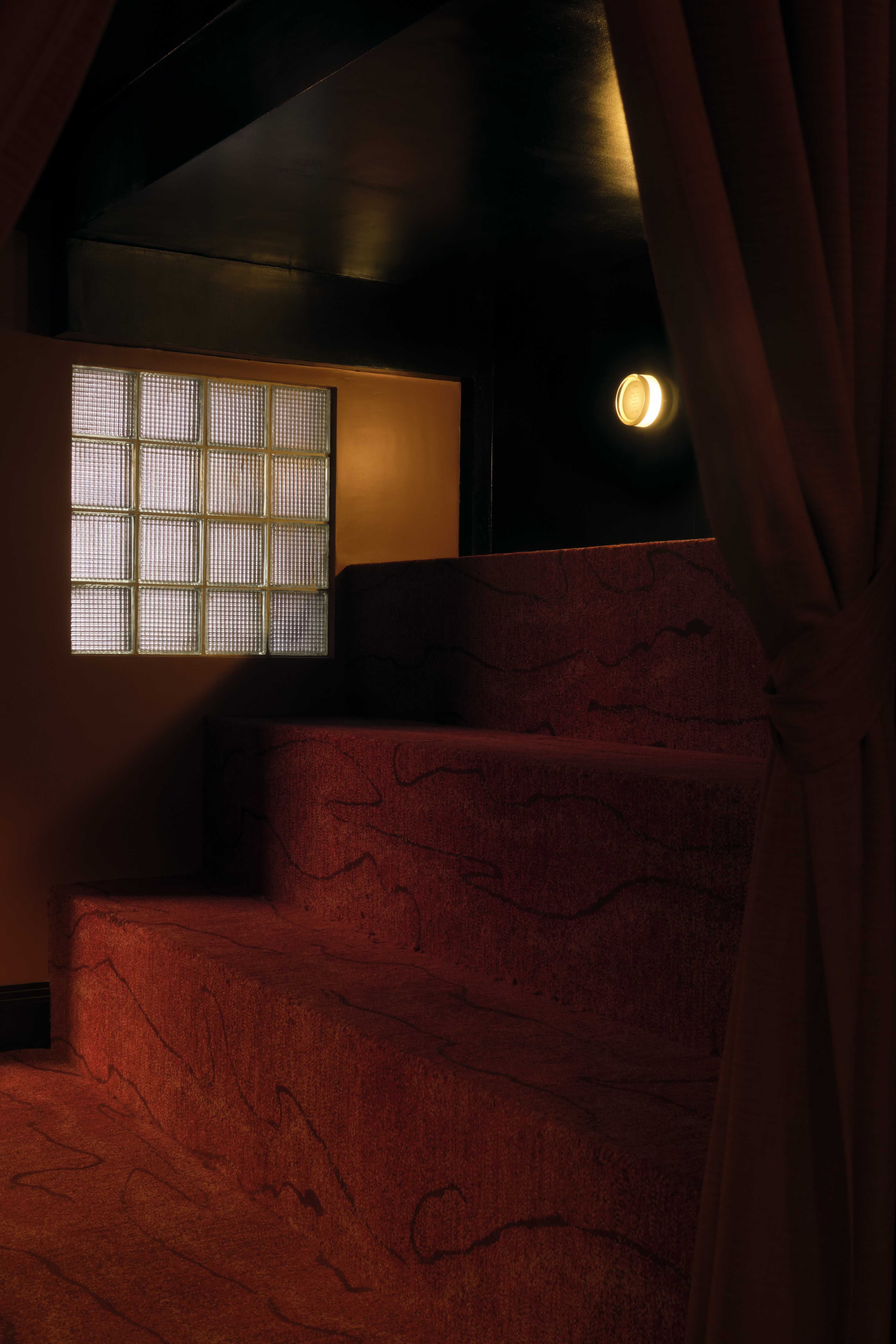 A golden-hued, dimly lit nightclub features velvety red or ochre plush fabrics, reflective surfaces, Art Deco-inspired sconces, and an air of mystery.