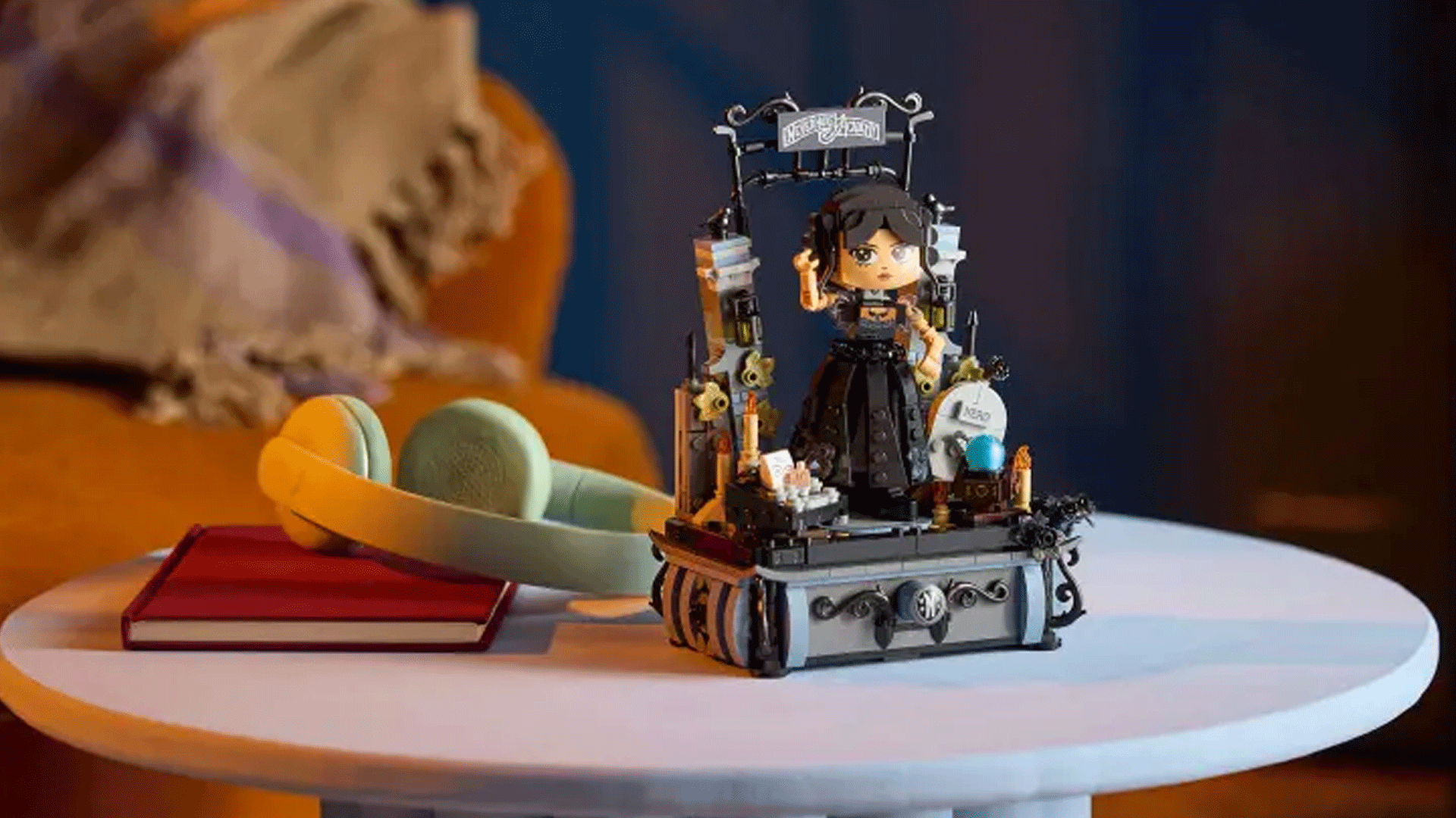 The Lego Wednesday Adams figure on a table next to some headphones and a book