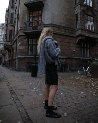 Jeanette Madsen in a grey sweater, black shorts, black socks, and ballet flats.