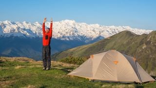 A man doing yoga next to his tent in the mountains
