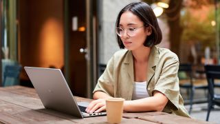 Dell laptop being used by a person sat at a table outside a coffee shop