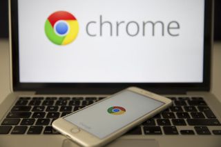 Google Chrome Logo on a laptop with a smartphone resting on its its keys also displaying the Chrome logo