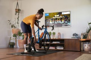 A woman mounting a bike to a Zwift Hub trainer