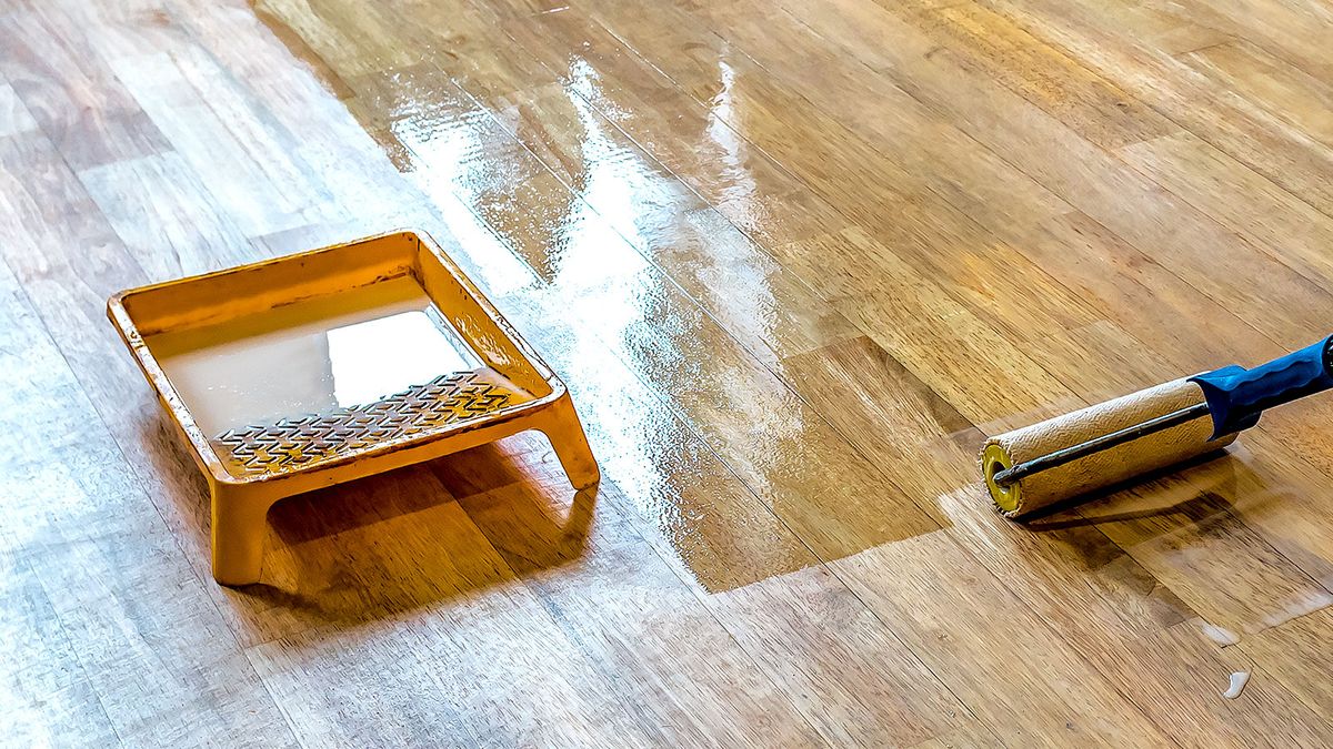 Roller tray and roller on pole painting varnish onto a dark wooden floor