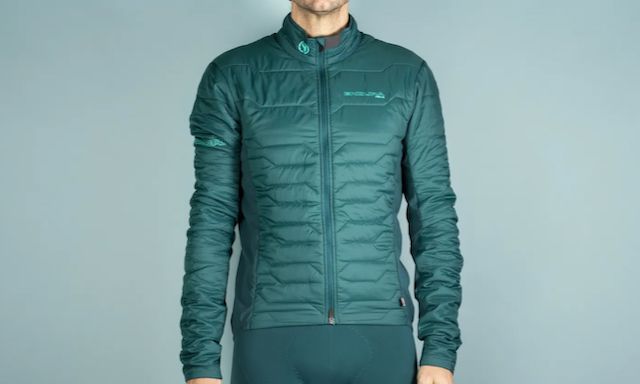 A white man in a green insulated jacket stands in front of a green background