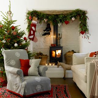 A living room decorated for Christmas with a Christmas tree and a garland draped around an alcove for a wood burning stove