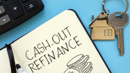 Notebook in which "cash-out refinance" is written sitting next to a pair of house keys and a calculator