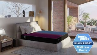 A bedroom scene featuring an Eight Sleep mattress with a black base and a dual-colored (red and blue) thermal top cover, implying temperature regulation. The mattress is on a gray upholstered bed frame. The room has modern, minimalist decor with large windows offering a view of an outdoor patio area with white furniture. A Tom's Guide Black Friday Mattress Deals logo is overlaid in the bottom right corner.