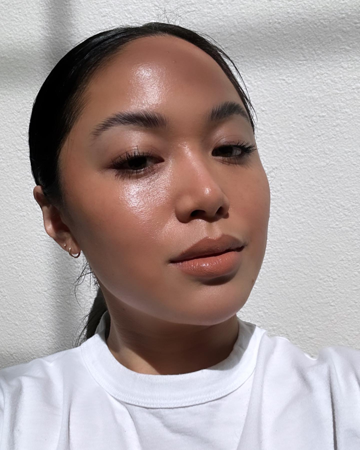 Photo of a woman taking a selfie wearing a white T-shirt with glowing skin