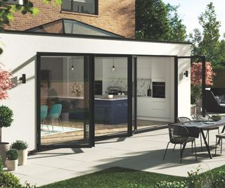 The exterior of a single storey extension with black framed bi-folding doors and outdoor furniture on a patio