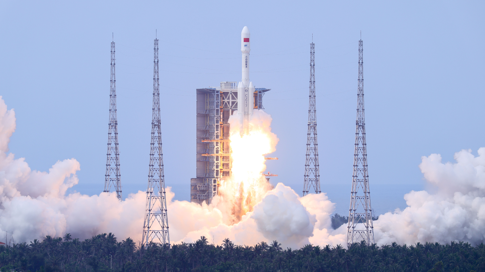 A photo of a Long March 7 rocket lifting off from a forest in China during the day