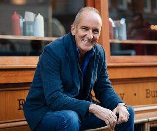 Kevin McCloud smiling sitting on a bench