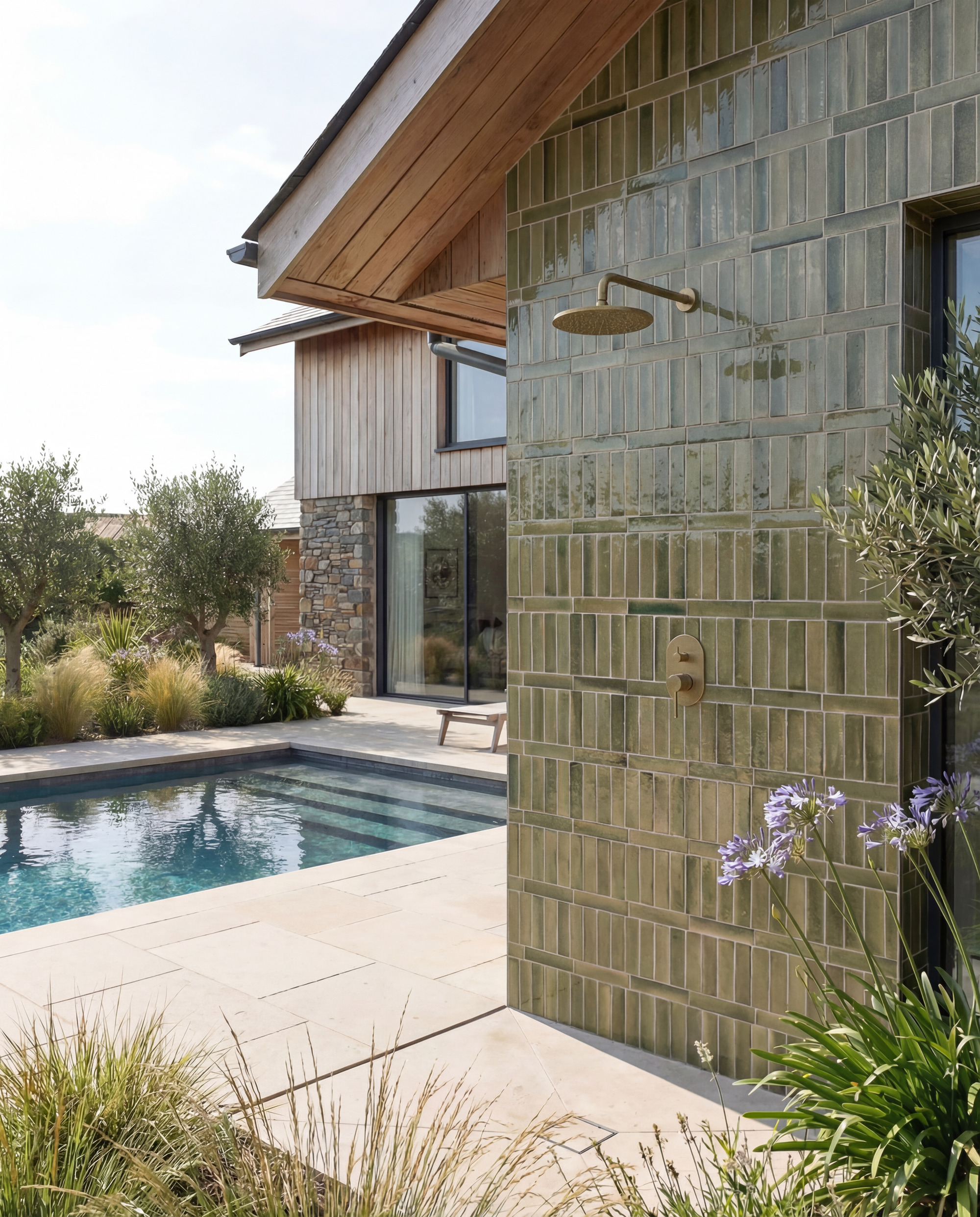 outdoor shower next to pool with green tiles by Ca' Pietra and brass shower with agapanthas