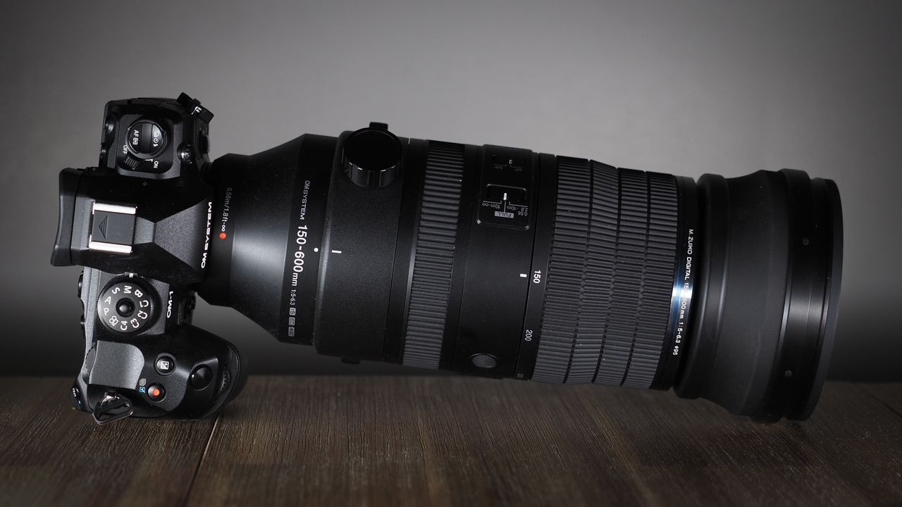 OM System M.Zuiko 150-600mm f/5.0-6.3 IS lens, mounted to an OM System OM-1 Mark II, on a wooden surface lit with moody lighting