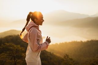 A women with braided hair running across a hilly landscape at sunset