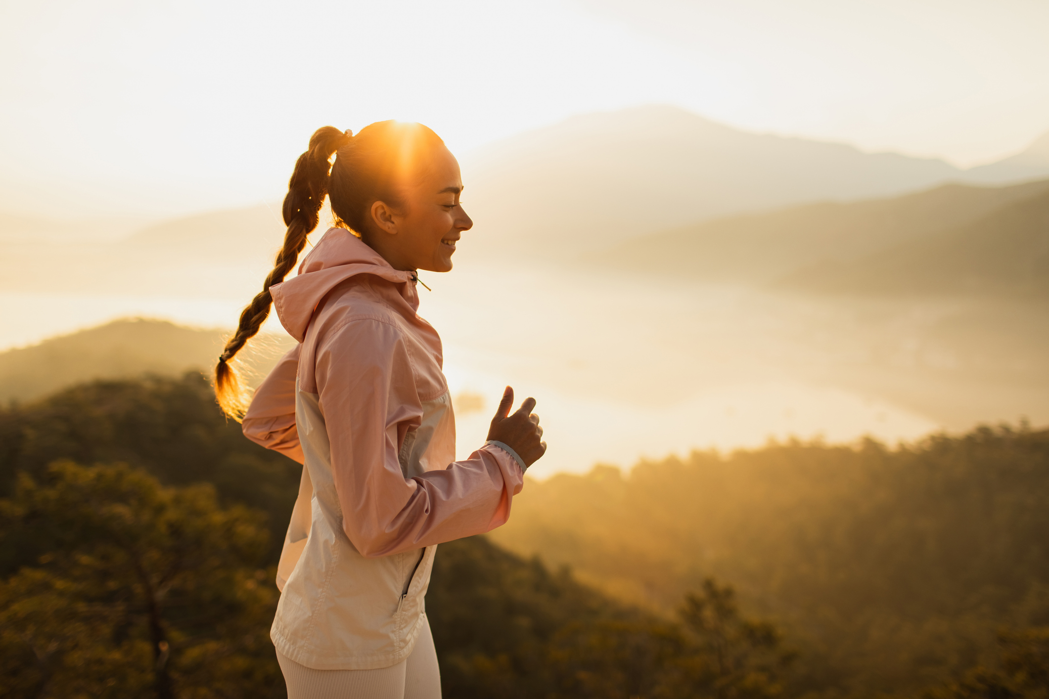 A women with braided hair running across a hilly landscape at sunset