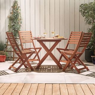A round wooden outdoor table and four chairs in front of a fenced patio area