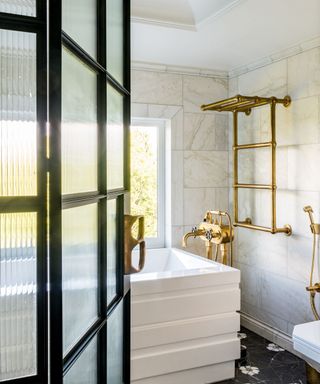 A white bathtub with gold fixtures behind a black metal and glass door