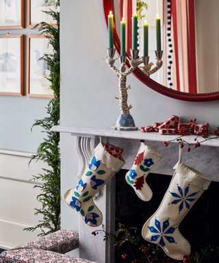 Christmas stockings hanging from a mantelpiece with lit candles in a candlestick in front of the mirror.
