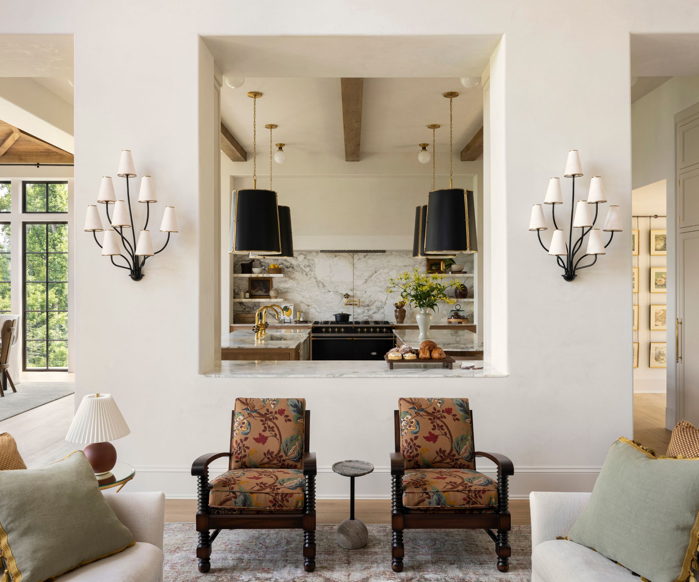 A warm white living room with a large pass-through window into a wood and marble kitchen