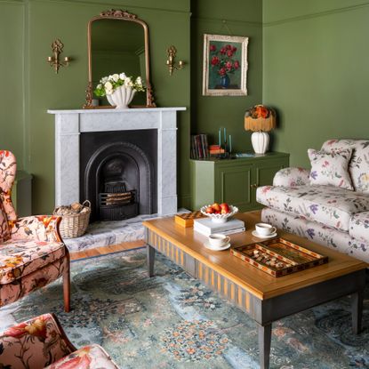 A green colour-dreched living room with a floral-print sofa and two pink floral-print armchairs facing it
