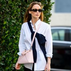 Jennifer Lawrence walks down the street wearing Dior's Cigale handbag with a white button-down shirt, black trousers and black flip-flips.