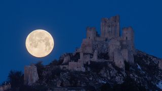 a bright moon rises above the ruins of a castle
