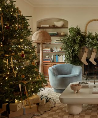 neutral living room with a christmas foliage fireplace and a large christmas tree sat on a checkerboard rug with a tree skirt and gifts