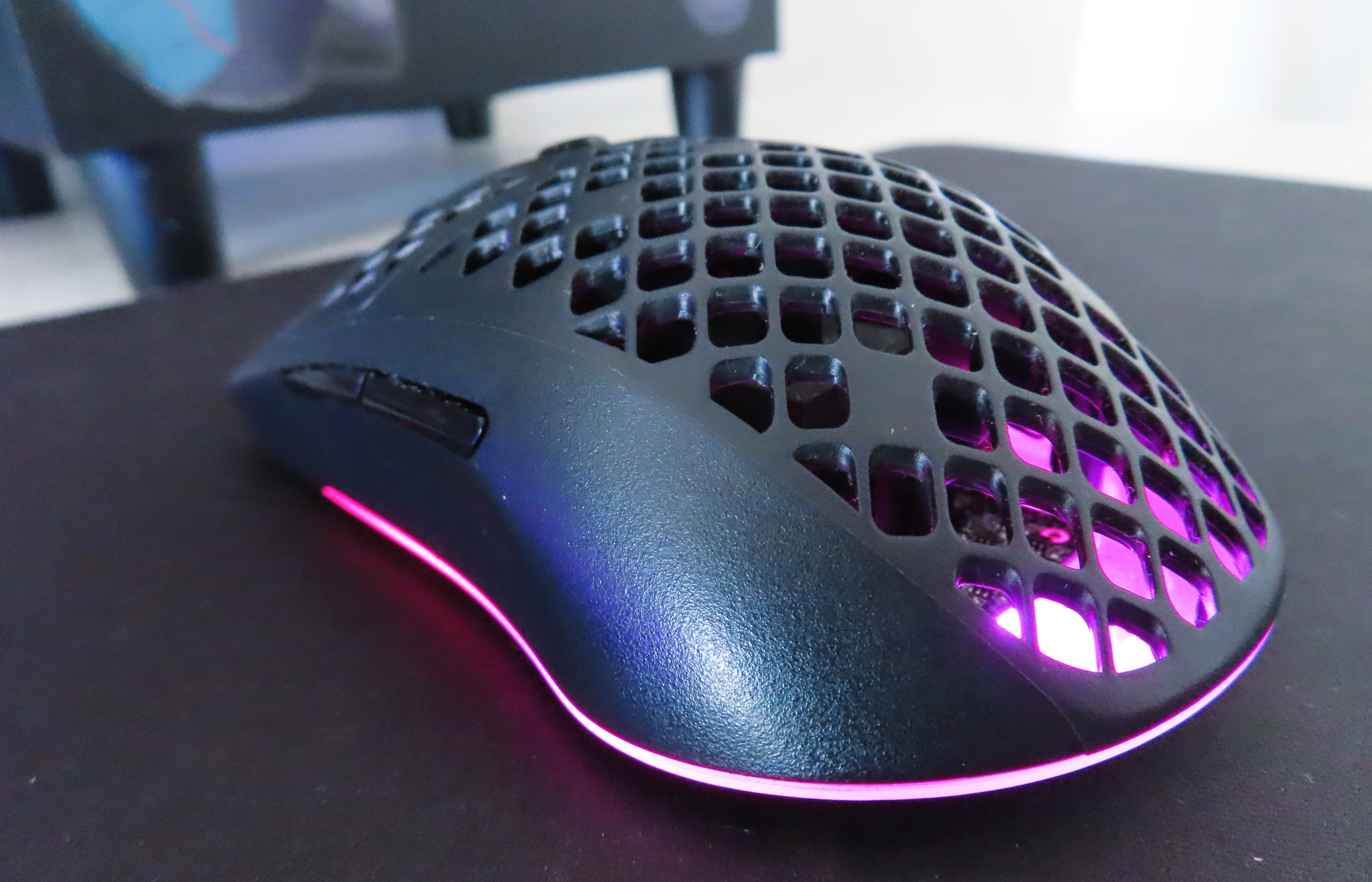 En svart SteelSeries Aerox 3 ligger på en svart musmatta med RGB-belysningen aktiverad.