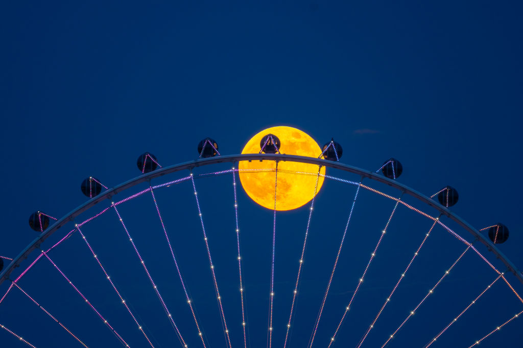 A deep orange sphere behind a round steel structure with silver spokes