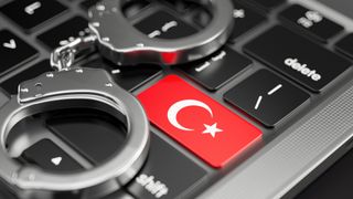 Handcuffs lying on a keyboard. The keyboard's enter key features the T&uuml;rkiye flag.