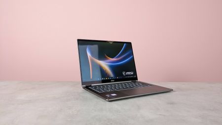 Three-quarter view of MSI Prestige 14 Flip AI+ open on white desk with pink wall in background