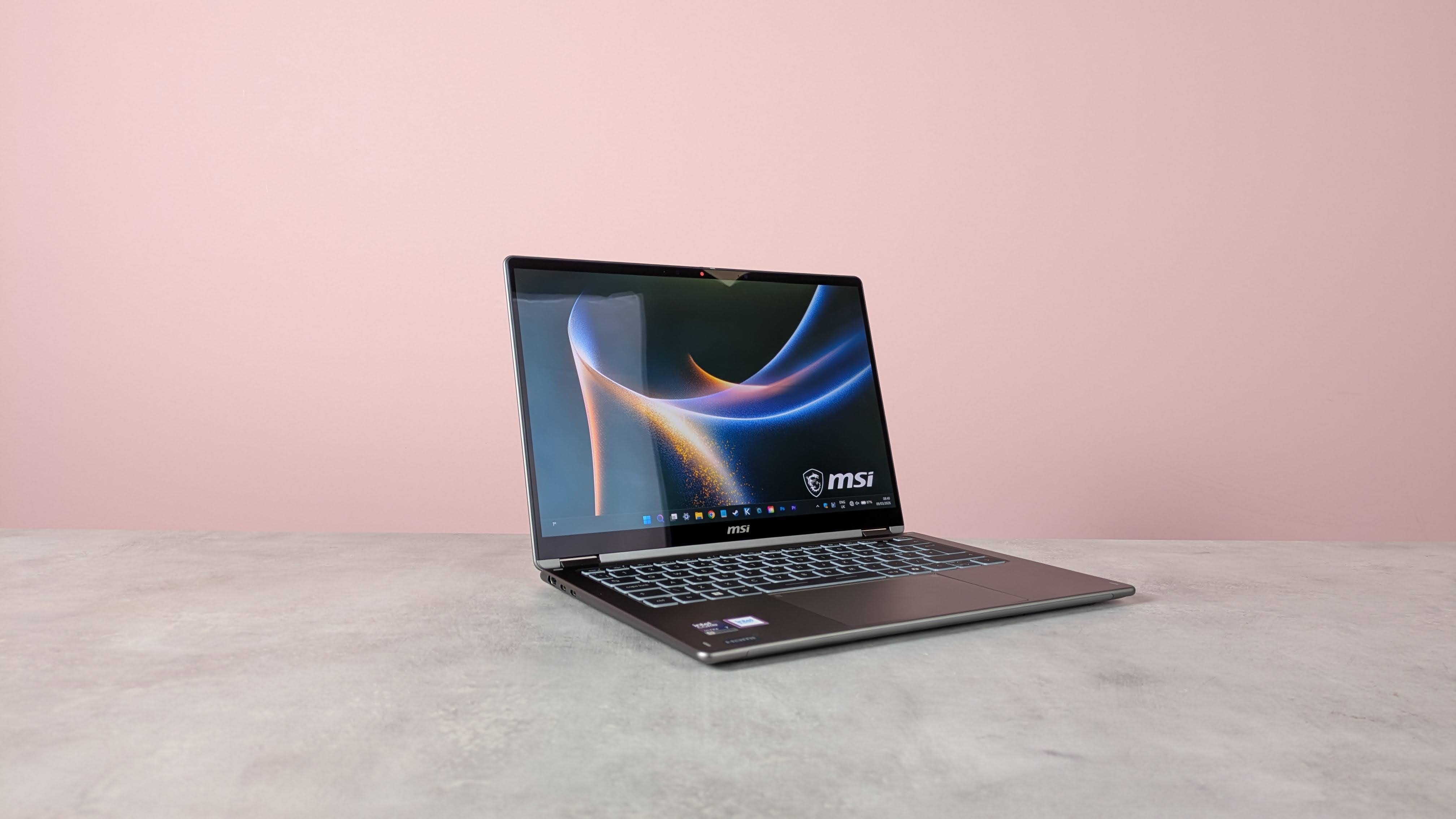 Three-quarter view of MSI Prestige 14 Flip AI+ open on white desk with pink wall in background