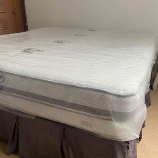 mattress with no bedding covered in plastic in a white room