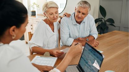 An older couple talk with another woman at a table while looking at paperwork.