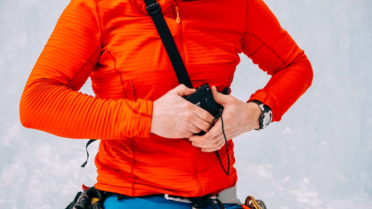 Close up of an ice climber putting on an avalanche beacon while at the base of a frozen waterfall 