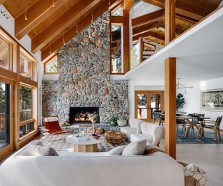 living room with vaulted roof fire in stone fireplace white sofas and view of lake