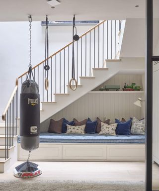 Hallway with staircase, punchbag suspended from the ceiling beside rings, wooden flooring and rug.