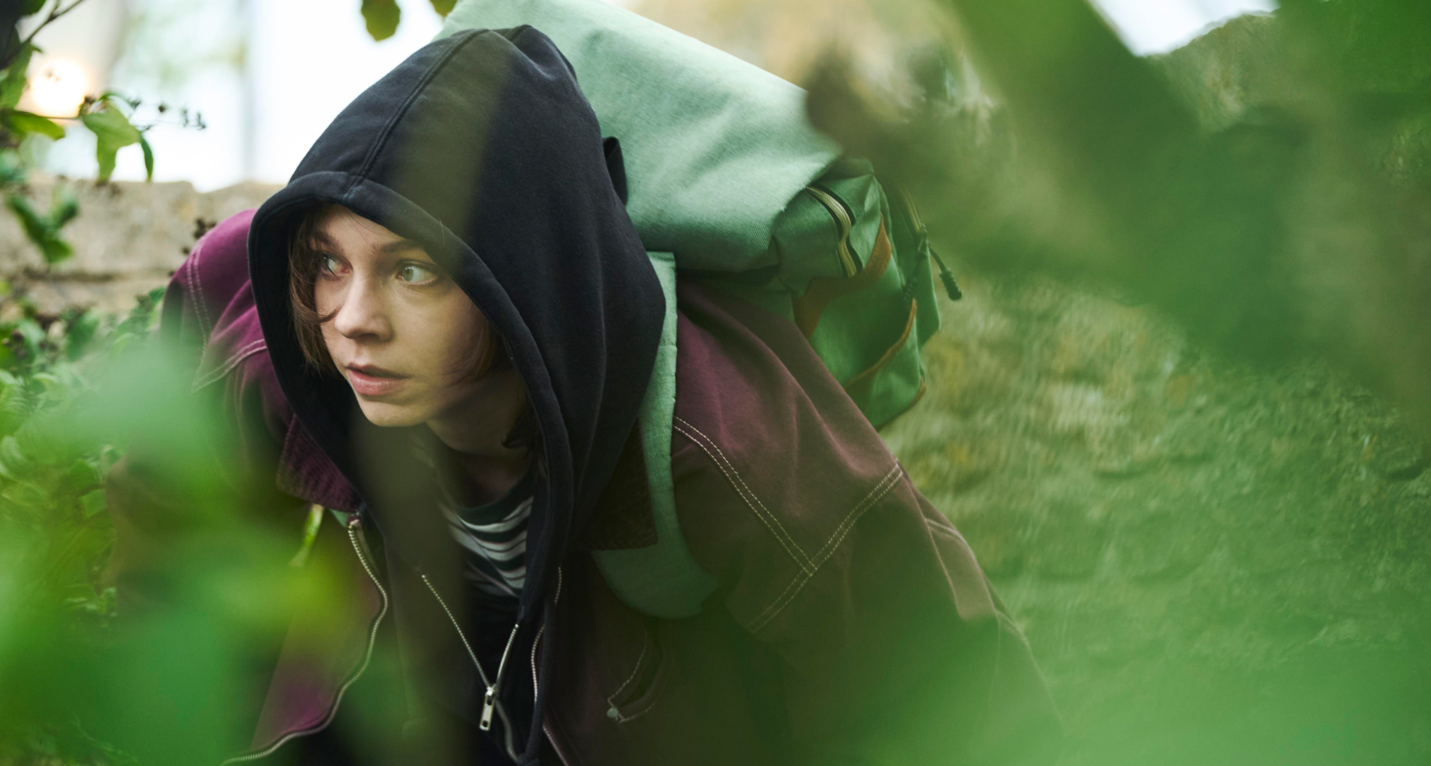 emma myers as pip wearing a hoodie purple jacket and backpack as she hides in grass in a good girl#039;s guide to murder season 3