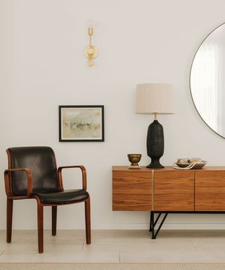 Wooden console with accent fabric and wooden chair, table lamp and large round mirror on the wall