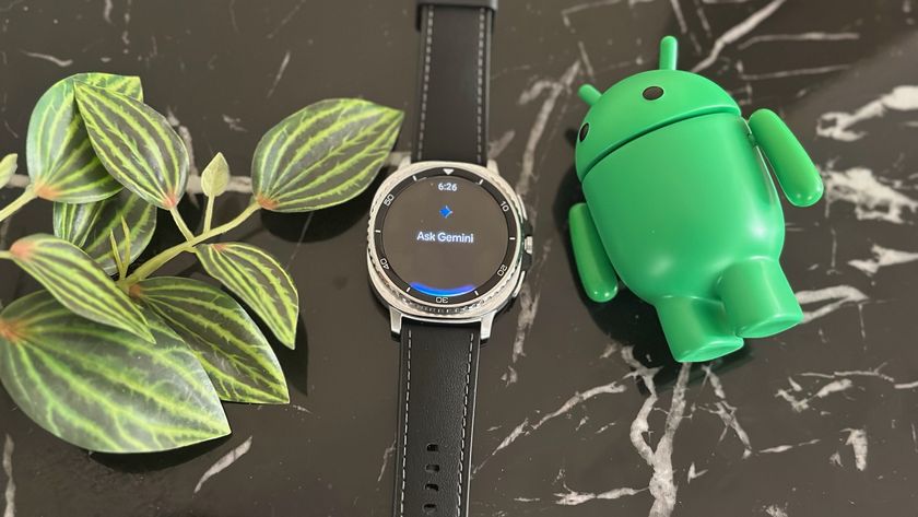 The Gemini app on the Samsung Galaxy Watch 8 Classic, which lays on a black marble table next to plant leaves and an Android mascot figurine.